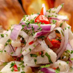Świeże ceviche z kawałkami ryby, czerwoną cebulą, kolendrą i pikantną papryczką, podane w szklanej misce.