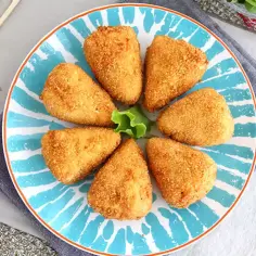 Siedem chrupiących kawałków camembert w panierce ułożonych na talerzu z niebieskimi wzorami. Idealna przekąska!