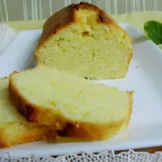 Szybka babka wilgotna, pokrojona na plastry, prezentuje się apetycznie na białym talerzu. Obok leży plaster cytryny.