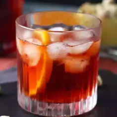 Klasyczny negroni przepis: czerwony koktajl z lodem i pomarańczą w szklance, obok pistacje.