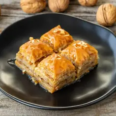 Słodka baklava na czarnym talerzu, otoczona orzechami. Idealny przepis na domową baklawę.