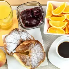 Pyszne śniadanie kontynentalne: rogaliki z cukrem pudrem, dżem, pomarańcze, sok i kawa.