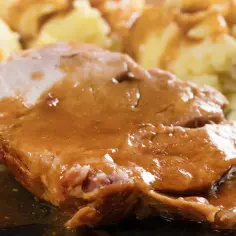 Mięciutka karkówka w sosie, podana z purée ziemniaczanym. Danie wygląda apetycznie i soczyście.