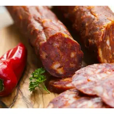 Chorizo co to? Pikantna, wędzona kiełbasa z papryką i kawałkami tłuszczu, obok czerwonej papryczki i natki pietruszki.