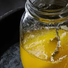 Słoik z żółtym płynem i widocznymi kryształkami, na ciemnym tle.