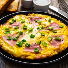 Pyszny omlet wytrawny z szynką i szczypiorkiem, podany na czarnym talerzu, obok grzanek.