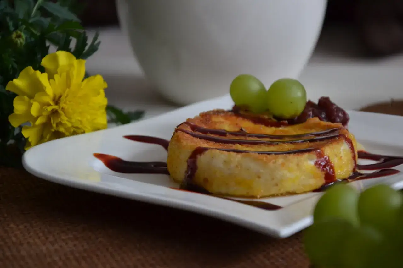 Złocisty camembert w panierce, polany sosem, z winogronami i żurawiną. Obok żółty kwiat.