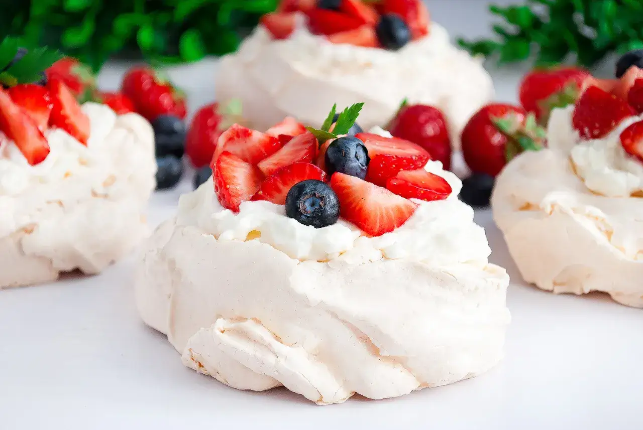 Beza pavlova która zawsze wychodzi, udekorowana bitą śmietaną i świeżymi truskawkami oraz borówkami.