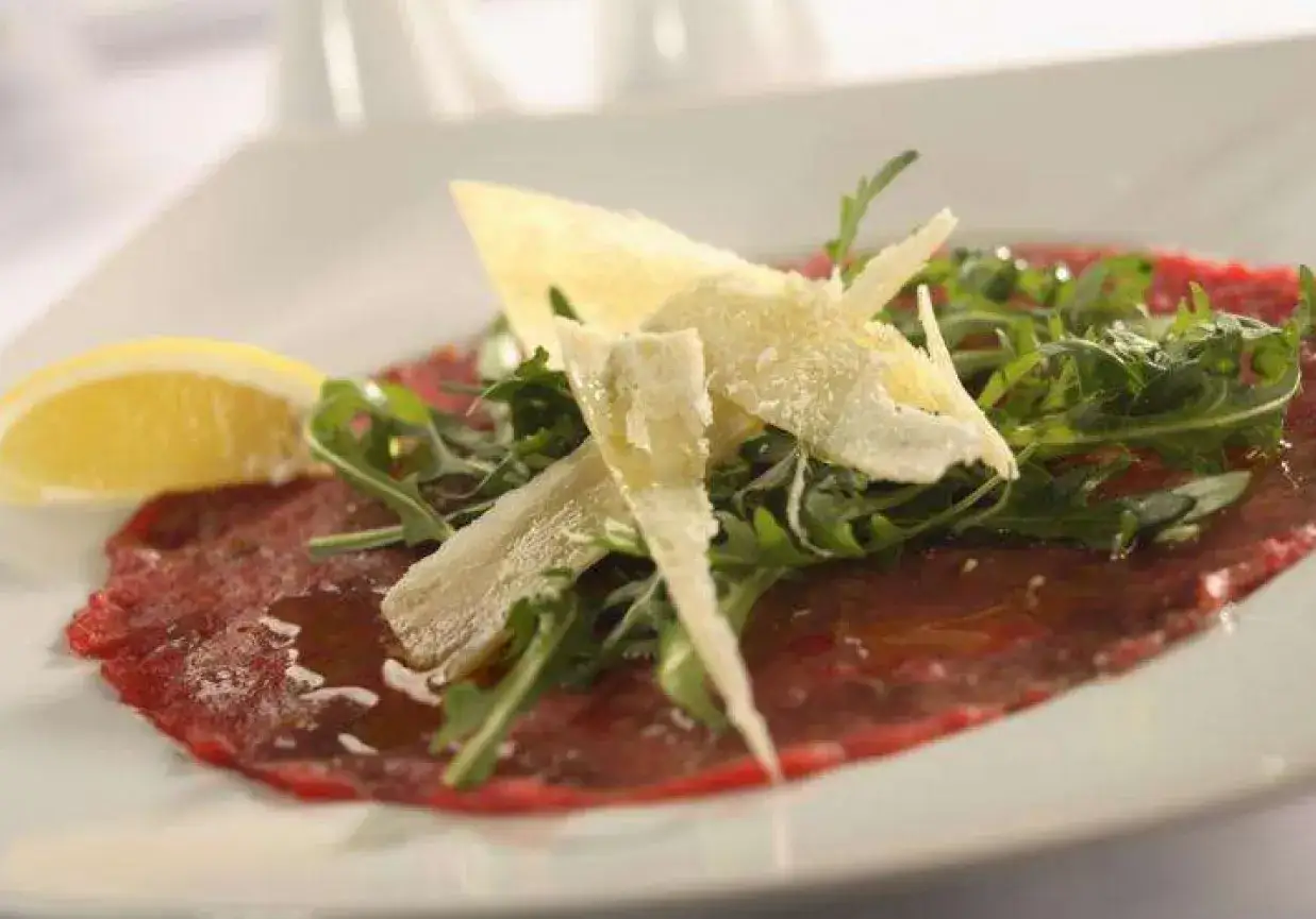 Eleganckie carpaccio z wołowiny z rukolą, płatkami parmezanu i plasterkiem cytryny.