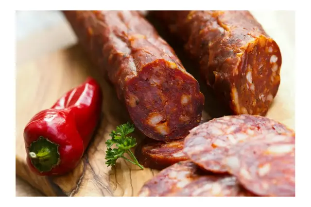Chorizo co to? Pikantna, wędzona kiełbasa z papryką i kawałkami tłuszczu, obok czerwonej papryczki i natki pietruszki.