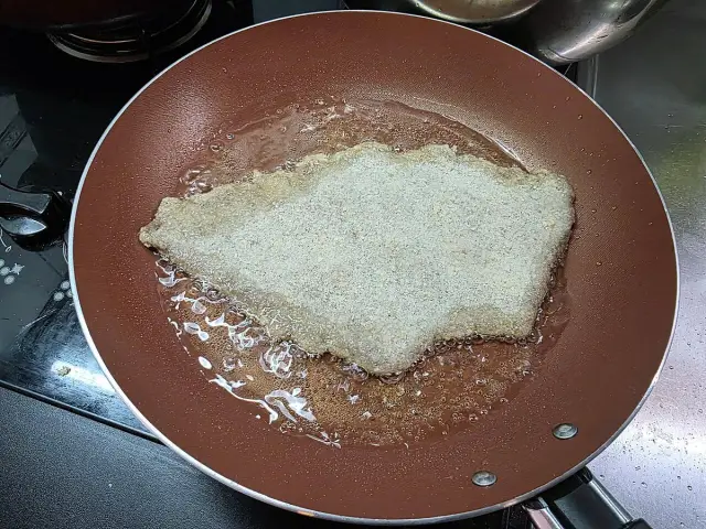 Kotlet w panierce smaży się na patelni w złocistej oliwie z oliwek do smażenia.